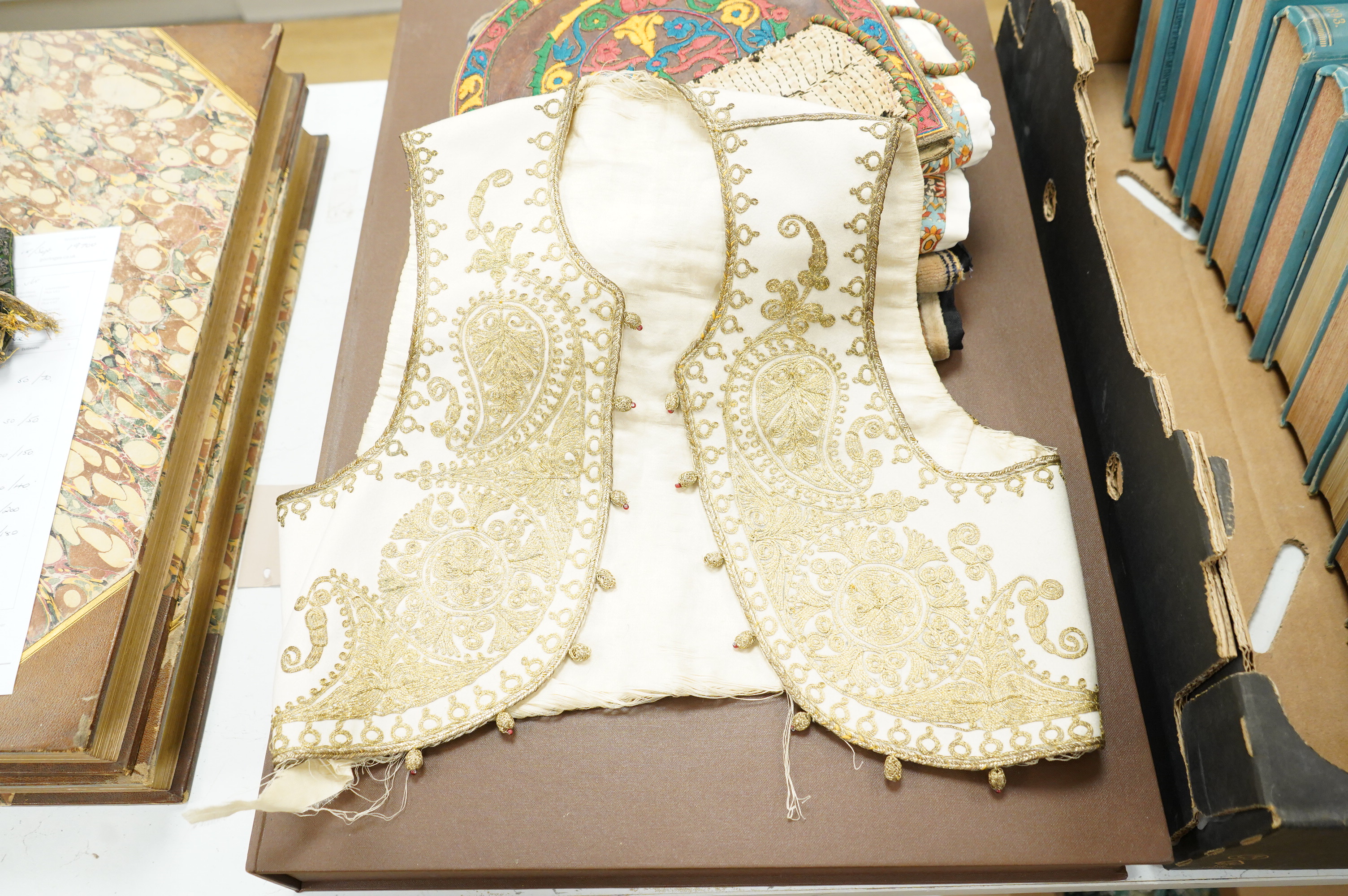 A collection of 20th century textiles to include: child's cream and gold embroidered waistcoat, a metallic embroidered bag, a leather embroidered bag, two Art Deco printed velvet cushion covers, a cotton quilted runner a